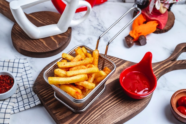 Top view french fries in a basket with ketchup on the board