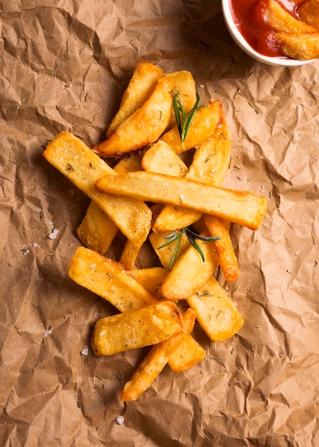 Top view of french fries on paper with herbs and ketchup