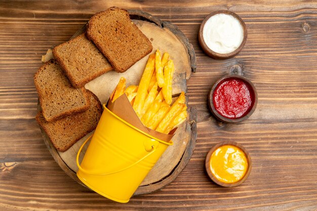 Top view of french fries with dark bread and seasonings on brown table