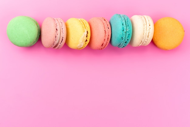 Free photo a top view french macarons colorful round delicious lined on pink, cake biscuit confectionery