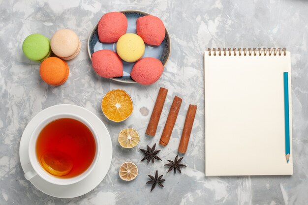 Top view french macarons with little cakes and cup of tea on light white surface cake biscuit sugar sweet pie tea