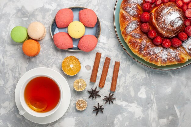 Top view french macarons with little cakes strawberry pie and cup of tea on white surface cake biscuit sugar sweet pie tea