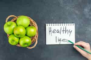 Free photo top view fresh apples in wicker basket healthy life written on notepad pencil in woman hand on dark surface