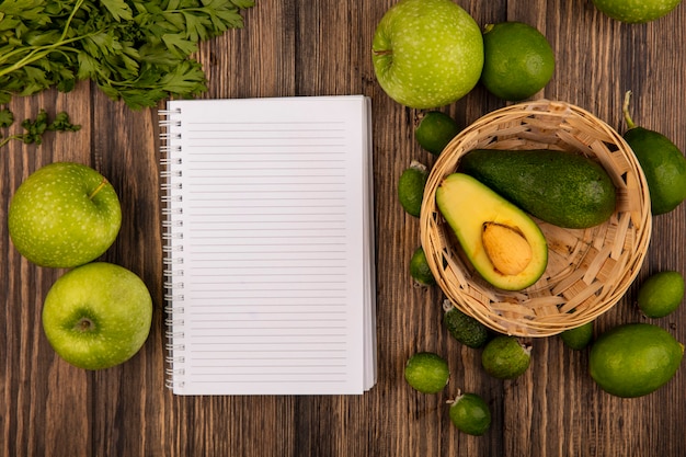 Top view of fresh avocados on a bucket with green apples limes feijoas and parsley isolated on a wooden background with copy space