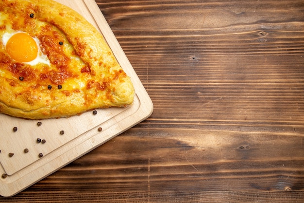 Top view fresh baked bread with cooked egg on brown wooden background dough breakfast egg bun food