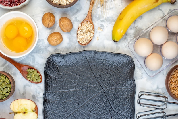 Top view of fresh banana wooden spoon walnuts oats in a brown pot and black tray eggs on ice background