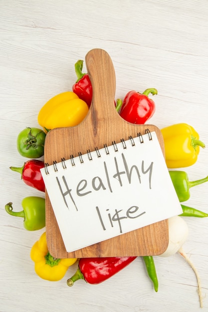 Free photo top view fresh bell-peppers different colored with brown wooden desk on a white background salad diet ripe color photo healthy life