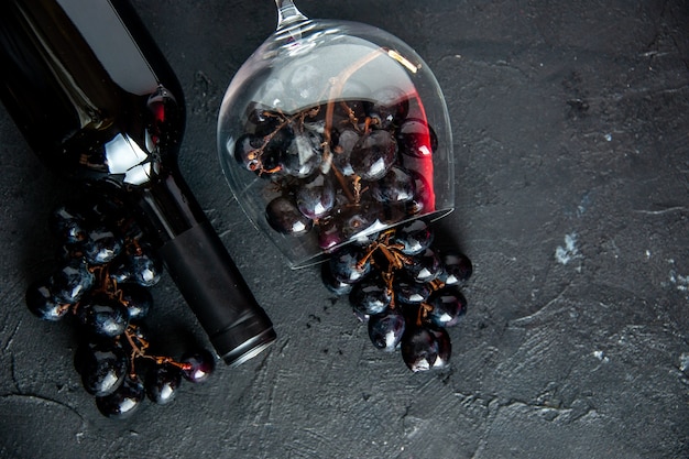 Top view fresh black grapes in wine glass wine bottle on dark background