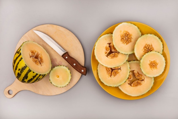 Free photo top view of fresh cantaloupe melon on a wooden kitchen board with knife with melon slices on a yellow plate on a white wall