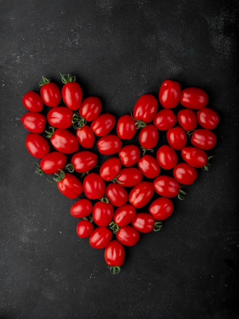 Top view of fresh cherry tomatoes arranged in a heart shape on black background