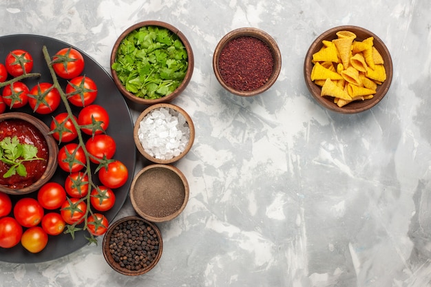 Top view fresh cherry tomatoes inside plate with different seasonings on white desk