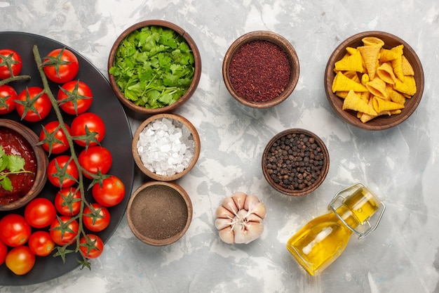 Top view fresh cherry tomatoes inside plate with different seasonings on white surface