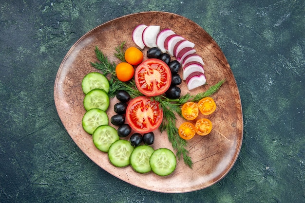 Top view of fresh chopped vegetables olives kumquats in a brown plate on green black mixed colors background