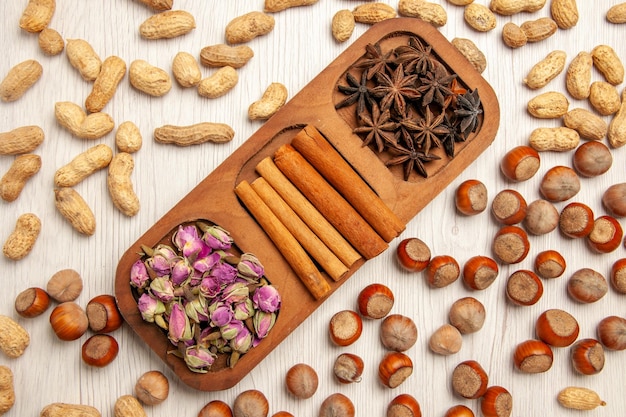 Top view fresh cinnamon with flowers and different nuts on white desk flower plant color