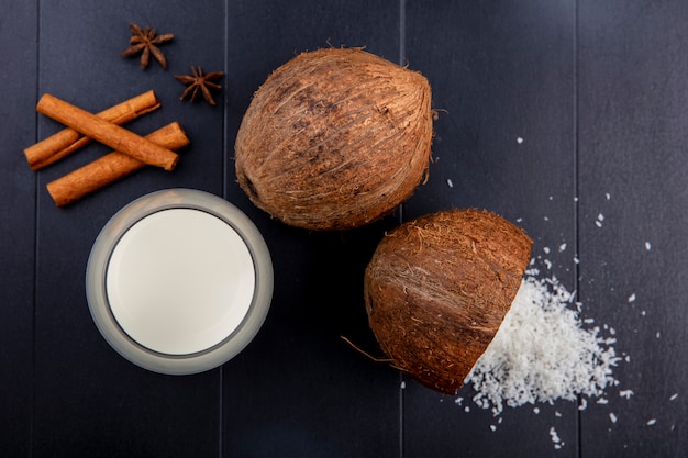 Top view of fresh coconuts with cinnamon stick with a glass of milk with a powder of coconut on wood