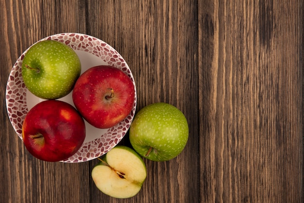 Top view of fresh and colorful apples on a bowl with green apples isolated on a wooden wall with copy space