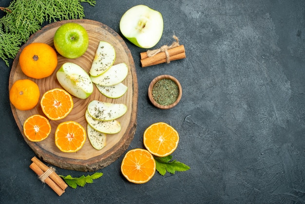 Free photo top view fresh cut apples and oranges dried mint powder in bowl cinnamon sticks on wood board on black table