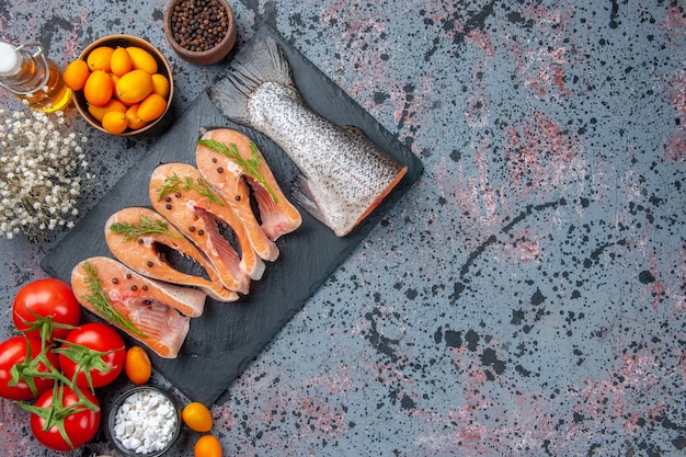 Free photo top view of fresh cut raw fishes green on dark color tray spices kumquats oil bottle on blue black mix colors table