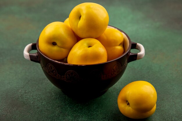 Top view of fresh delicious peaches on a bowl on a green background