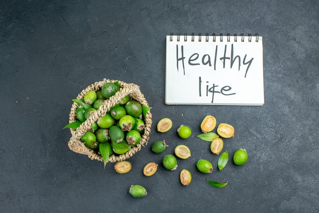 Free photo top view fresh feijoas in basket healthy life written on notebook on dark surface