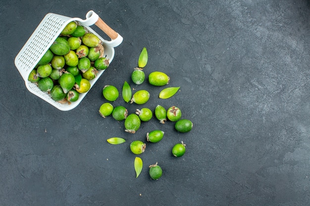 Top view fresh feijoas scattered from plastic basket on dark surface with copy space