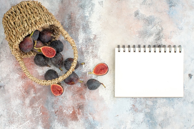 Free photo top view fresh figs scattered from basket a notebook on nude background