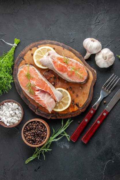 Top view fresh fish slices with lemon and garlic on dark table