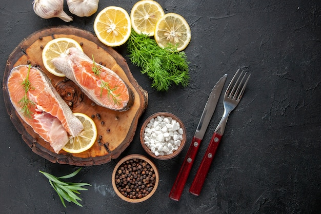 Top view fresh fish slices with lemon slices on dark table