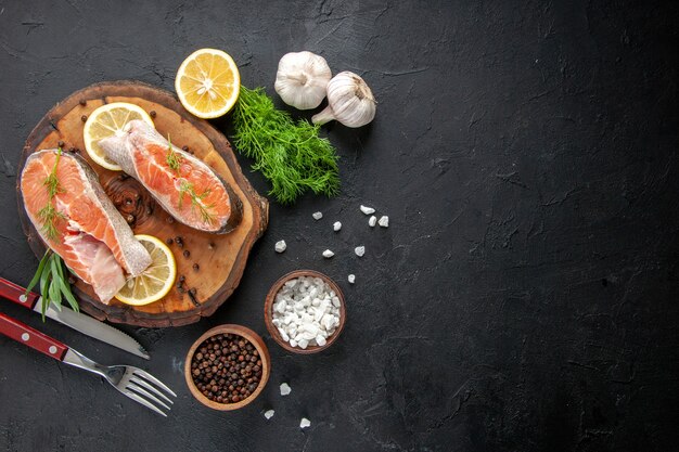 Top view fresh fish slices with lemon slices and garlic on dark table