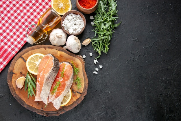 Top view fresh fish slices with lemon slices garlic and seasonings on a dark table