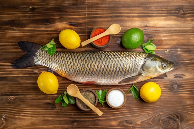 Top view fresh fish with lemon and seasonings on wooden desk