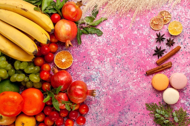 Top view fresh fruit composition with french macarons on light-pink surface