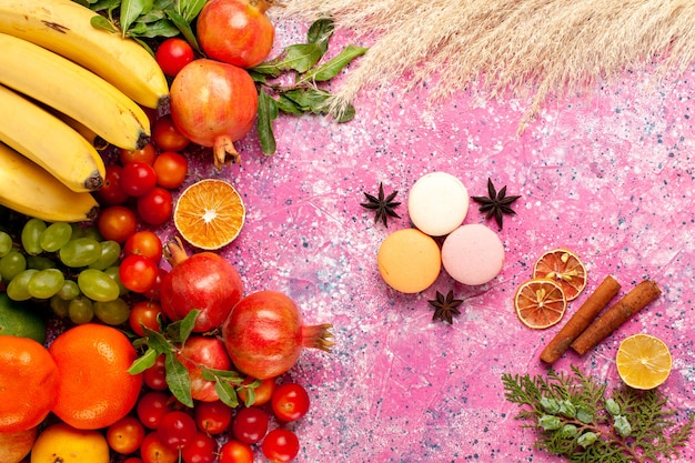 Top view fresh fruit composition with french macarons on light-pink surface