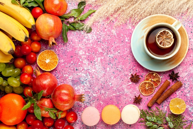 Top view fresh fruit composition with french macarons and tea on light-pink surface