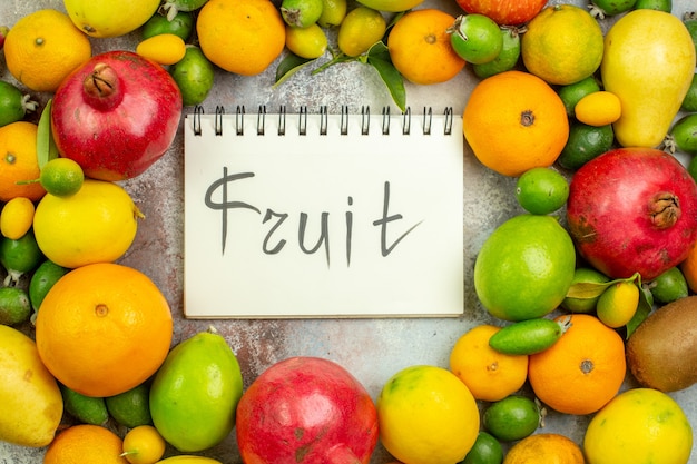 Top view fresh fruits different mellow fruits with fruit written notepad on white background tasty berry color diet  health ripe tree