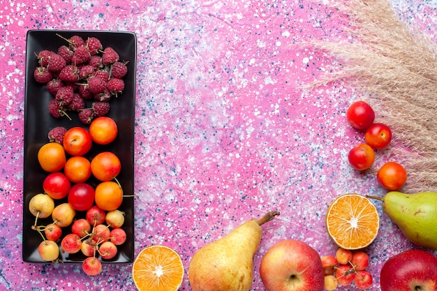 Top view of fresh fruits raspberries and plums inside black form on pink surface