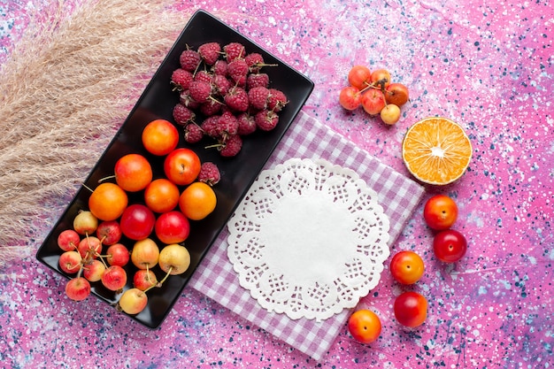 Top view of fresh fruits raspberries and plums inside black form on the pink surface