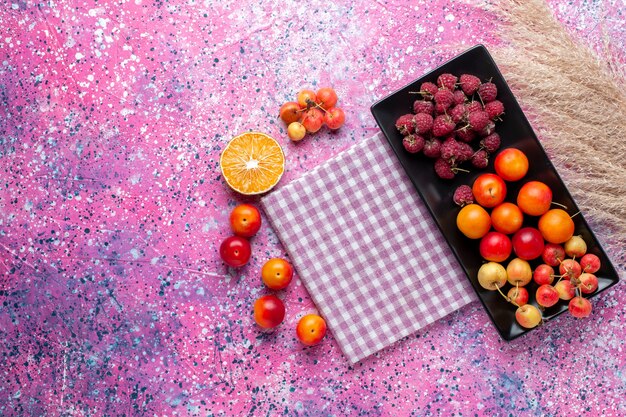 Top view of fresh fruits raspberries and plums inside black form on the pink surface