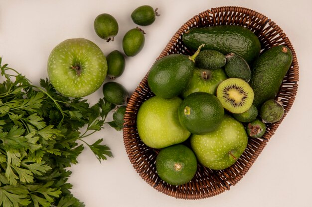 Top view of fresh fruits such as kiwi apples avocados limes and feijoas on a bucket on a white wall