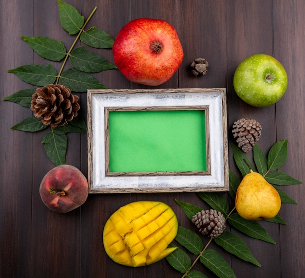 Top view of fresh fruits such as pomegranate green apple pear sliced mango isolated with leaf and pine cones on wood