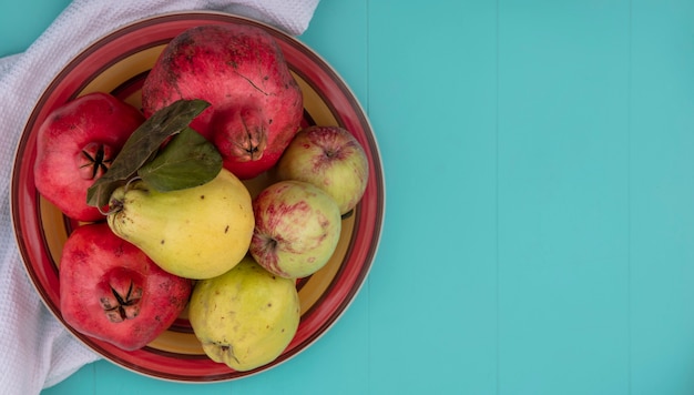 Free photo top view of fresh fruits such as pomegranate quince and apples on a bowl on a white cloth on a blue background with copy space