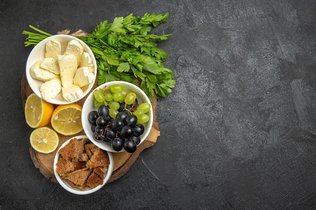 Top view fresh grapes with white cheese greens and lemon slices on the dark surface meal fruit milk food