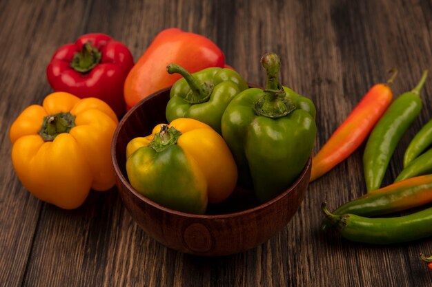 Top view of fresh green peppers on a bowl with colorful peppers isolated on a wooden surface