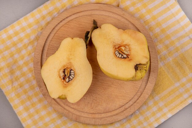 Top view of fresh halved quinces on a wooden kitchen board on a yellow checked cloth