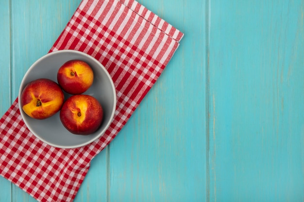 Top view of fresh juicy peaches on a bowl on a red checked cloth on a blue wooden wall with copy space