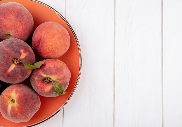 Top view of fresh and juicy peaches onn orange plate on white with copy space