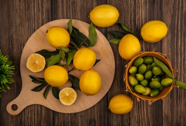 Top view of fresh lemons isolated on a wooden kitchen board with kinkans on a bucket on a wooden background