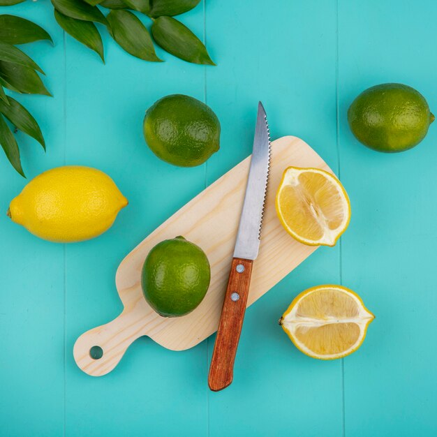 Top view of fresh lemons on wood kitchen board with knife and leaves on blue