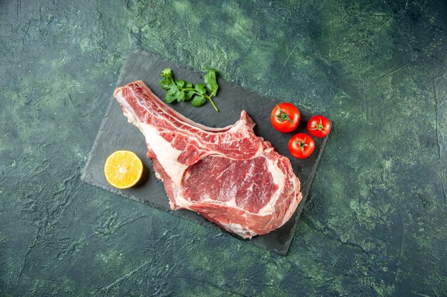 Top view fresh meat slice with red tomatoes on dark-blue background kitchen animal cow food butcher meat color