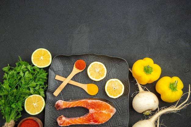 Top view fresh meat slices with greens lemon and seasonings on dark background